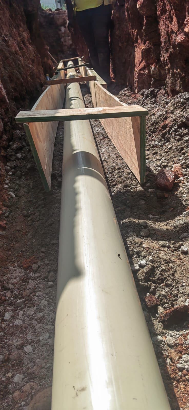 Pipe resting on bedding in a trench with timber supports